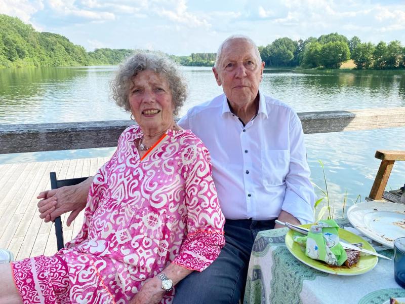 Das Eheparr Horstmann sitzt lächelnd an einem Tisch, im Hintergrund ein See.